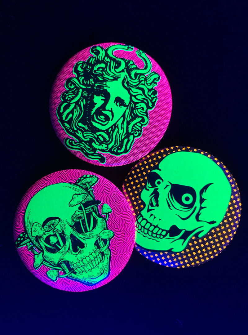 Neon badges glowing under black light, Medusa, Retro Skull, and Skull with Mushrooms growing out of eye sockets.